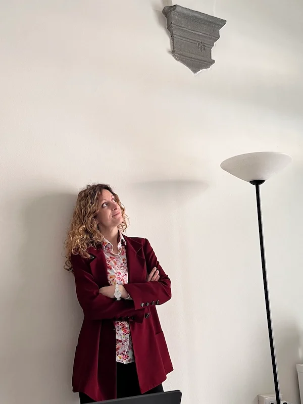 Foto profilo di Elena Valori architetto, nel suo studio con sguardo in alto appoggiata a parete bianca interna